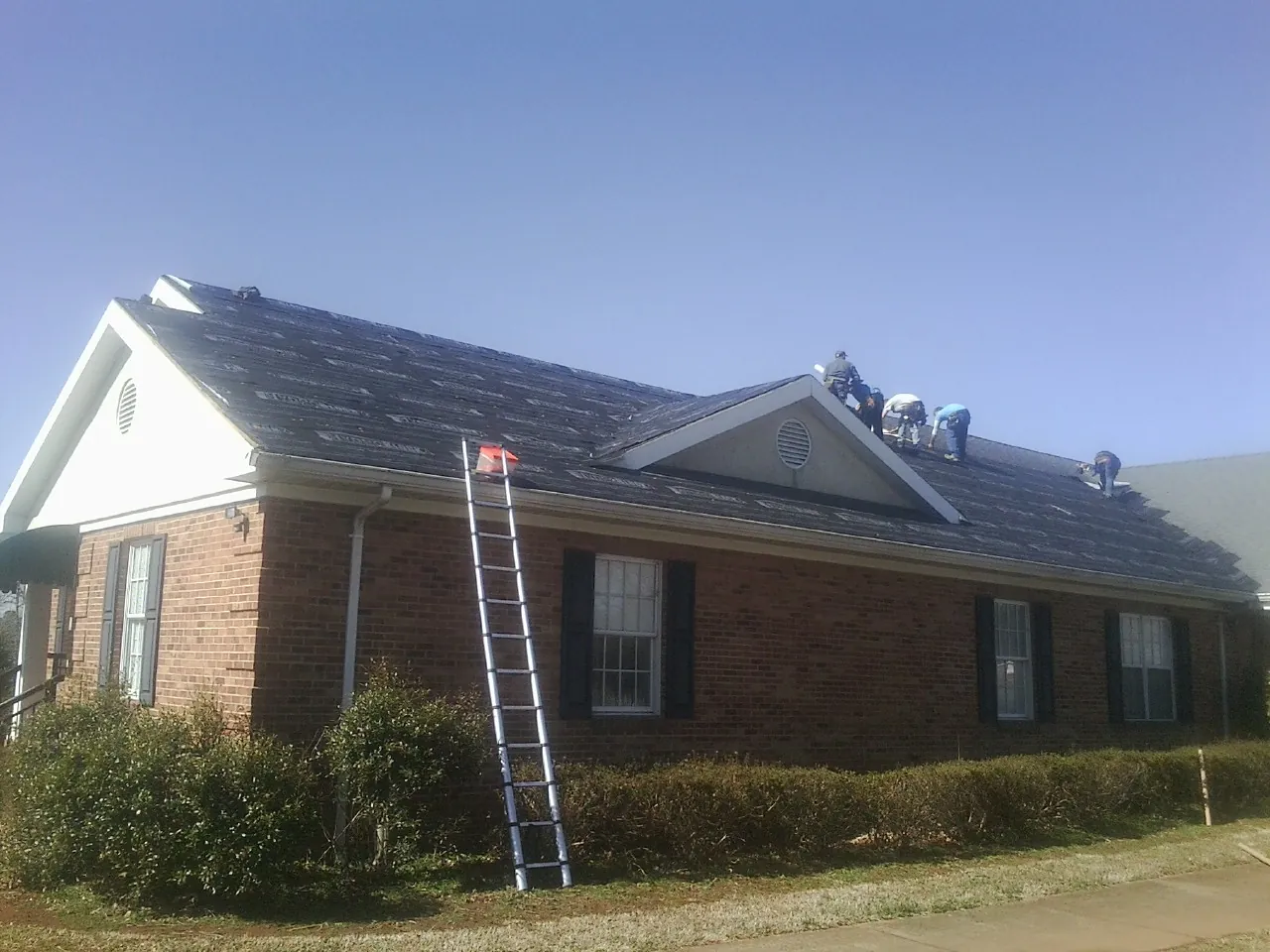 Crew tearing shingles off a brick ranch roof with a ladder set — Emergency Roof Repair work by our crew in Quaker City
