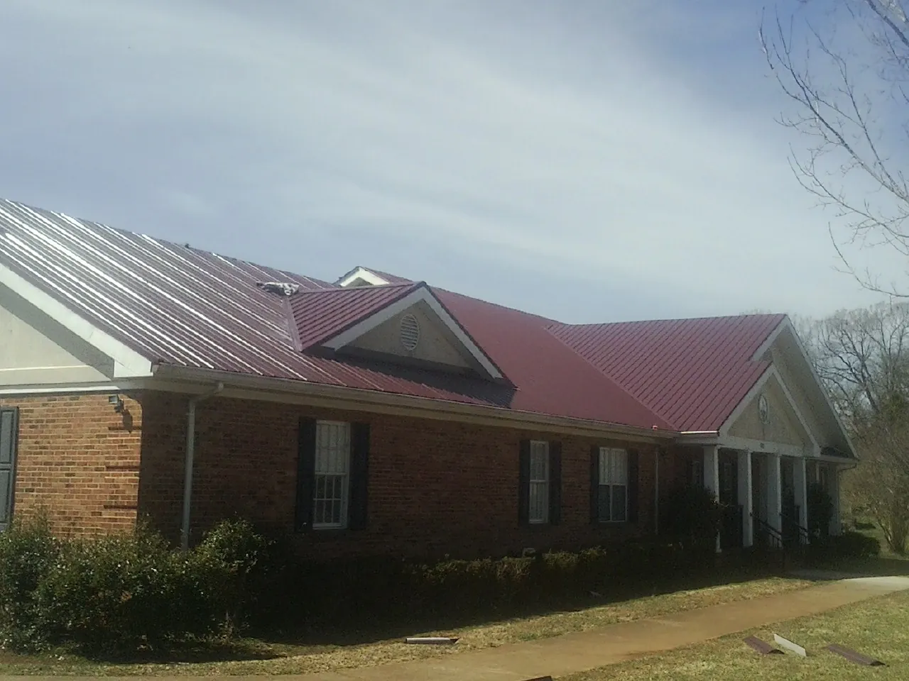 Red metal roof with gabled entries on a long brick building, from a Hail Damage Roof Repair job in Quaker City