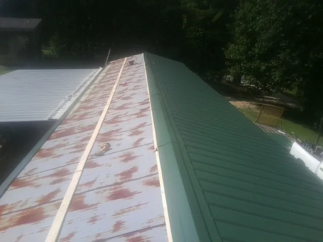 Old rusted panels beside newly installed green metal roofing — Wind Damage Roof Repair by Roofing Brothers in Quaker City