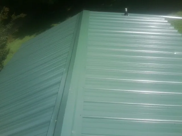 New green metal panels meeting at the ridge of a roof — Flat Roof Repair work by our crew in Quaker City