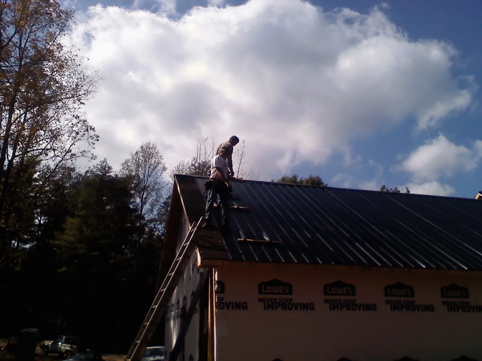 Roofer fastening dark metal panels high against a cloudy sky, from a Roof Inspection job in Quaker City
