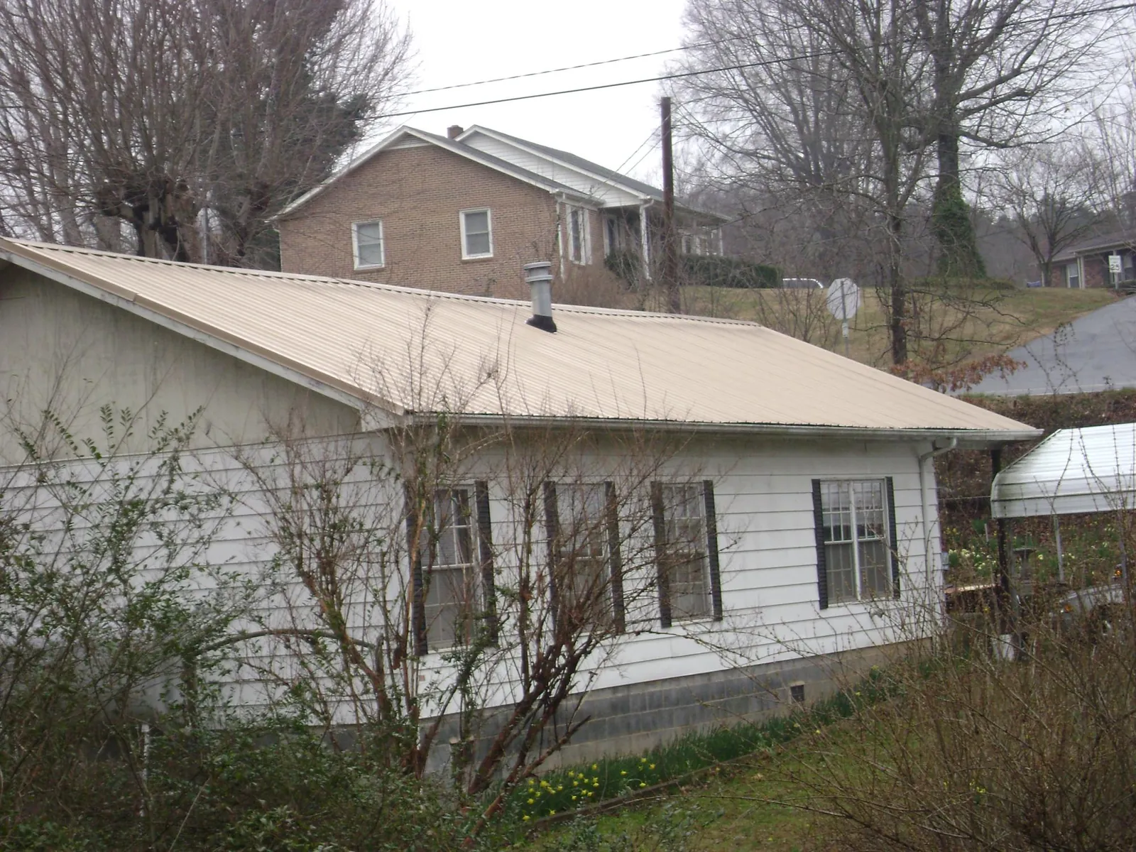 Tan metal roof on a white sided house set into a hillside — Commercial Roofing by Roofing Brothers in Quaker City