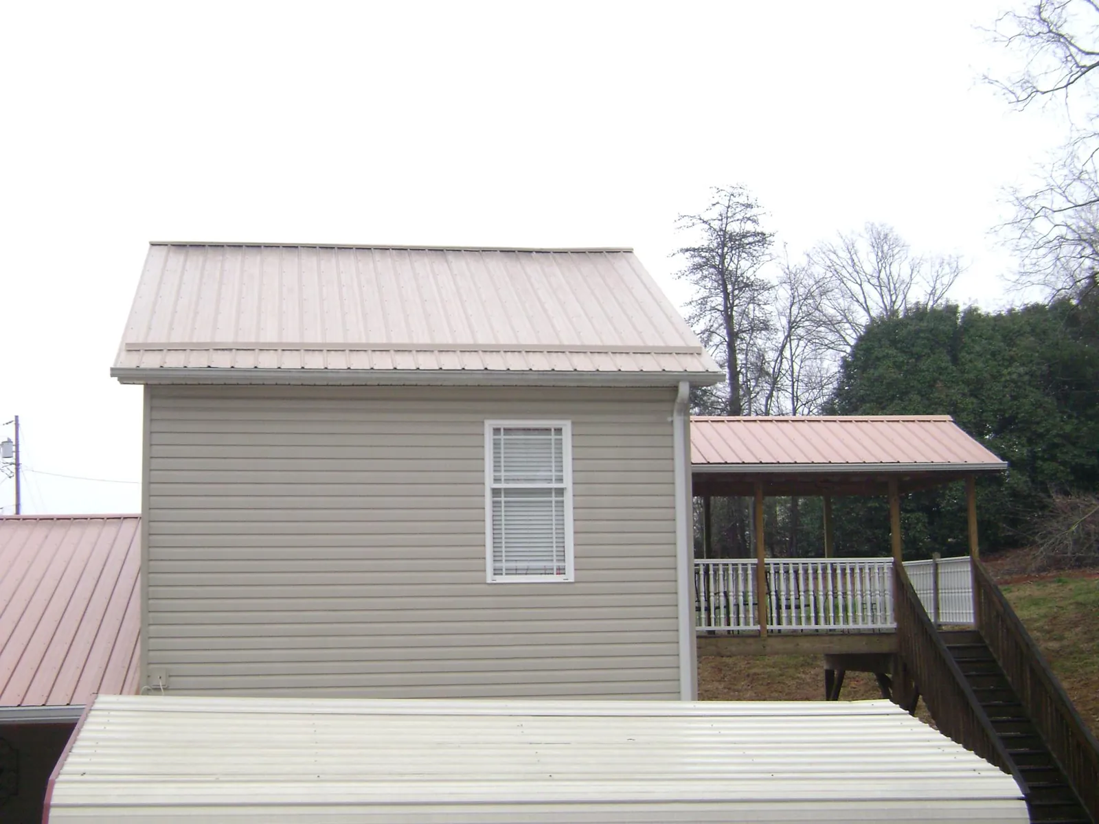 Tan metal roofs on a two story addition and attached porch, from a Roof Replacement job in Quaker City